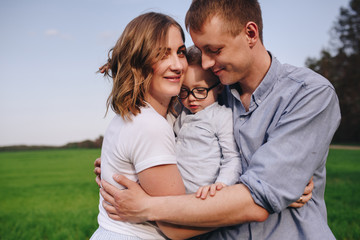 Family in the forest for a walk. Picnic in the meadow, on the green grass. Blue clothes. Mom, dad, son. Son on the hands of dad. A pet. Black Dog. The boy with glasses.