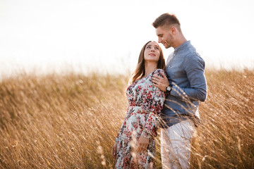 beautiful young couple hugging in a field with grass at sunset. stylish man and woman having fun outdoors. family concept. copy space.