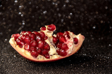 Juicy pomegranate on a black shiny background. Bright pomegranate berries.