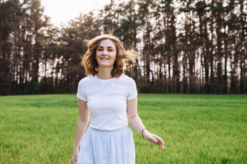 The girl is blonde, brown hair, in a white shirt and blue midi skirt. Walking in the field, through the green grass. Portrait of a girl. Positive and smile.