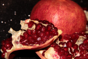Juicy pomegranate on a black shiny background. Bright pomegranate berries.