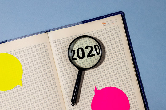 2020 inscription through a magnifying glass lying on a notepad with bright stickers. Year recap summary concept.