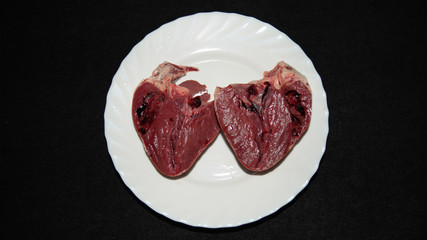 
Pork heart cut in half and placed in a white plate, on a black background