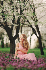 Beautiful blonde young woman in colorful flowers. girl with make-up and hairstyle in pink dress in blossoming spring park. woman's day