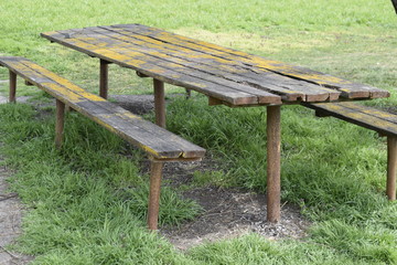 Wooden table and benches on rusty metal pipes. The wooden surface is covered with fungus and moss. Recreation area in nature.