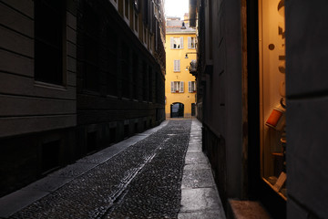 Narrow ancient street in the historical center of Milan city with nineteenth-century stone paving and yellow building in the end of the street. Italy traveling concept