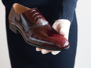 A gloved salesman offers shoes for fitting. Men's classic leather maroon shoes. Very expensive Executive shoes.