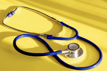 Blue stethoscope  on a yellow background with light and shadow. Medical equipment. Copy space....
