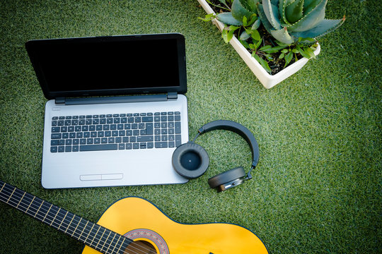 Learning and entertainment of six-string acoustic guitar with a laptop and headphones on a natural grass and plant background. Online guitar training. Distance music education