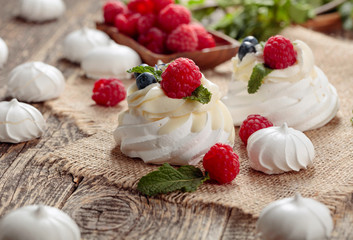 Dessert Pavlova with raspberries, blueberries and mint on a old wooden table.