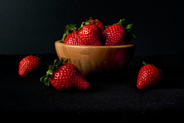 Wooden bowl with red strawberries inside and around on a black background