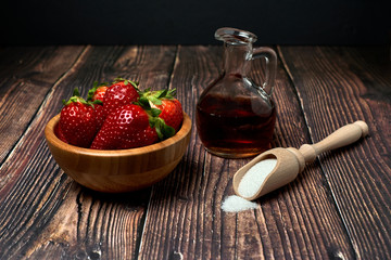 Wooden bowl with fresh red strawberries with sugar and vinegar for its preparation on a black background