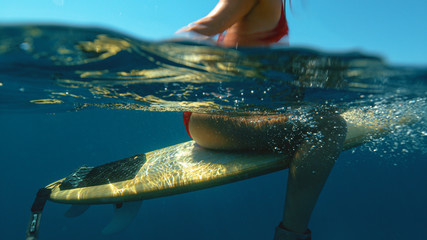 HALF IN HALF OUT: Young female surfer sits on her surfboard and waits in line up