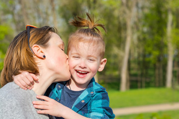 Fototapeta na wymiar Mom kisses her little boy, who laughing in the park