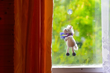 a child's stuffed toy hangs on a suction Cup on a window covered with rain