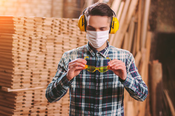 Portrait male carpenter in protective headphones on ears, medical mask on face wearing protective...