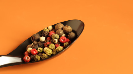 A mixture of hot, red, black, white and green peppers in a black spoon. Isolated on a brown background.