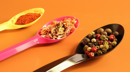 Various spices in plastic spoons on a brown background. Copy space. A mixture of peppers, red smoked paprika, seasoning twelve vegetables.