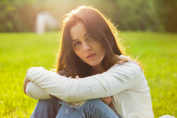 Obraz premium Beautiful girl sits on a meadow with grass in the sunlight. Her mood is joyful, happy, sad and tender. Femininity in all gestures. Happy woman's day. Summer