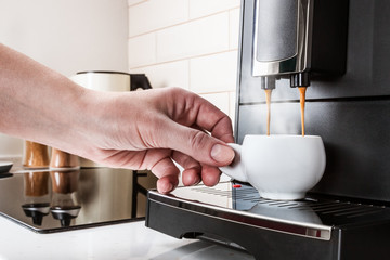 woman's hand picks up a white porcelain Cup of hot coffee from the coffee machine