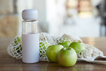 An eco bag with green apples and a bottle of water on a wooden table