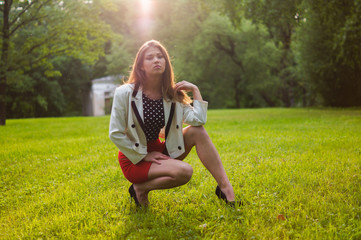 Fototapeta premium Beautiful and attractive girl is relaxing in the park on a summer day. Dressed and posing like a professional model with glasses and a red skirt
