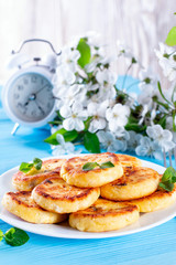 Cottage cheese pancakes or syrniki with mint on a blue background. Healthy breakfast or lunch