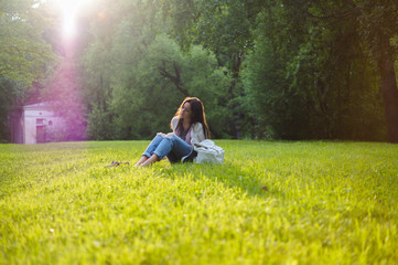 Beautiful girl sits on a meadow with grass in the sunlight. Her mood is joyful, happy, sad and tender. Femininity in all gestures. Happy woman's day. Summer