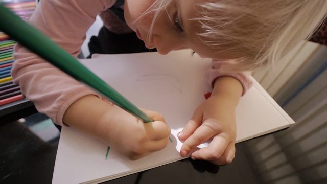 Child draws with colored pencils. Blonde caucasian girl draws fruit with colored pencil on black table at home. Close-up.