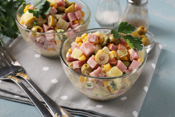 Salad with ham, olives, corn and pineapples in transparent salad bowls on a light blue background, Closeup