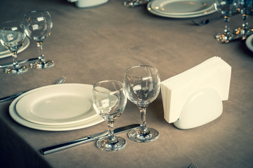 The served table in the restaurant. Clean dishes and appliances on the tablecloth in a cafe. Shiny transparent glasses. White plates. Prepared for the reception of guests. High service.