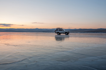 A beautiful car on the ice of Lake Baikal is reflected in smooth ice against a background of a beautiful bright sunset