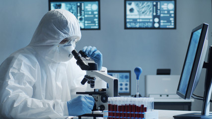 Scientist in protection suit and masks working in research lab using laboratory equipment:...