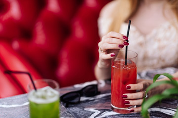 a girl in a beige dress drinks red juice in a restaurant on a red sofa
