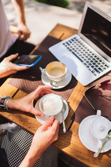 a interpreter for business meeting in a cafe. the girl is holding a coffee Cup, the man is holding a phone. there is a laptop on the table