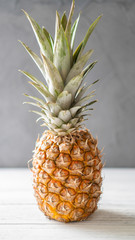 Single ripe illuminated pineapple on a white wooden table and gray background. Juicy standalone ananas.