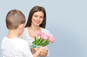 Little child son gives his mother a bouquet of delicate pink tulips. Mother's Day celebration.	