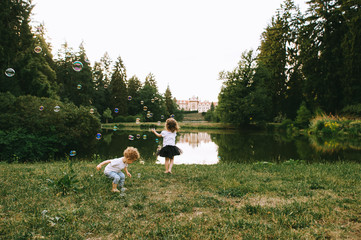 Two cute little children playing with bubles near the lake in sunny summer