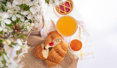 Romantic spring breakfast top view, flat lay. Orange juice, croissant, orange jam, pastry with spring white blossom flowers. Rustic style
