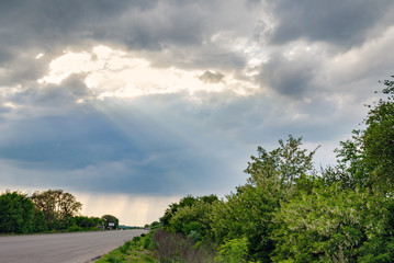 Fototapeta na wymiar the rays of the sun shine through the clouds on the road