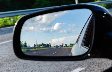 reflection of the road in the car mirror, with the sky and clouds, warm summer evening