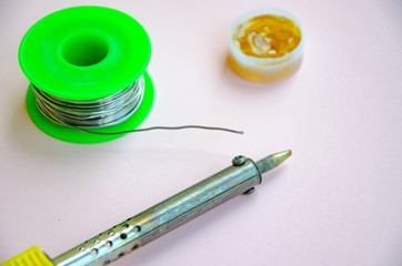 Soldering iron, tin, rosin on a pink background. Soldering iron in male hands. Macro. Repair of...