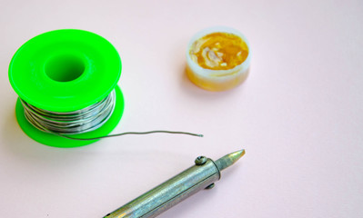 Soldering iron, tin, rosin on a pink background. Soldering iron in male hands. Macro. Repair of...