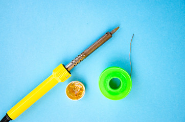 Soldering iron, tin, rosin on a blue background. Soldering iron in male hands. Macro. Repair of electrical equipment, radio engineering. Solder wires, contacts.  Copy Space