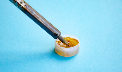 Soldering iron, tin, rosin on a blue background. Soldering iron in male hands. Macro. Repair of electrical equipment, radio engineering. Solder wires, contacts.  Copy Space