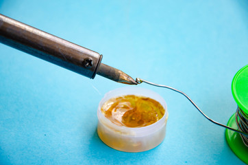 Soldering iron, tin, rosin on a blue background. Soldering iron in male hands. Macro. Repair of electrical equipment, radio engineering. Solder wires, contacts.  Copy Space