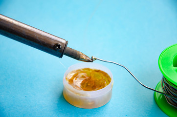 Soldering iron, tin, rosin on a blue background. Soldering iron in male hands. Macro. Repair of electrical equipment, radio engineering. Solder wires, contacts.  Copy Space
