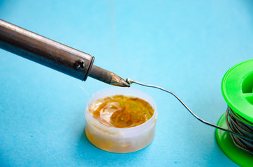 Soldering iron, tin, rosin on a blue background. Soldering iron in male hands. Macro. Repair of electrical equipment, radio engineering. Solder wires, contacts.  Copy Space