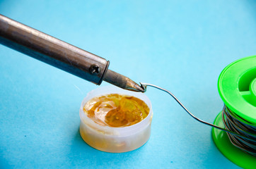 Soldering iron, tin, rosin on a blue background. Soldering iron in male hands. Macro. Repair of electrical equipment, radio engineering. Solder wires, contacts.  Copy Space