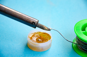 Soldering iron, tin, rosin on a blue background. Soldering iron in male hands. Macro. Repair of...